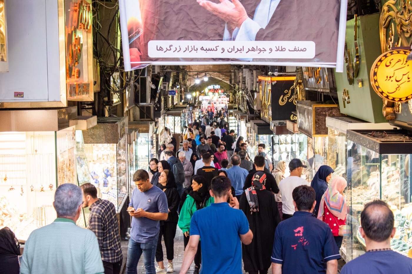 خریداران در راهروی طاقدار و شلوغ بازار بزرگ تهران، با مغازه‌های جواهرفروشی